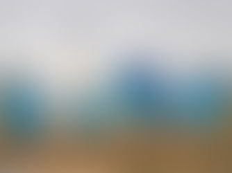 Five people in vibrant, colorful masks and blue ponchos dance energetically in a muddy field, with a drone hovering above, creating a surreal and lively scene.