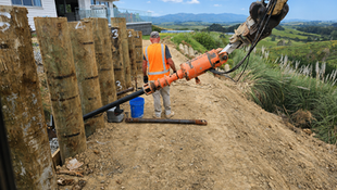 CIVILCO worker operating piling equipment beside a timber retaining wall for an Auckland slip repair consent project