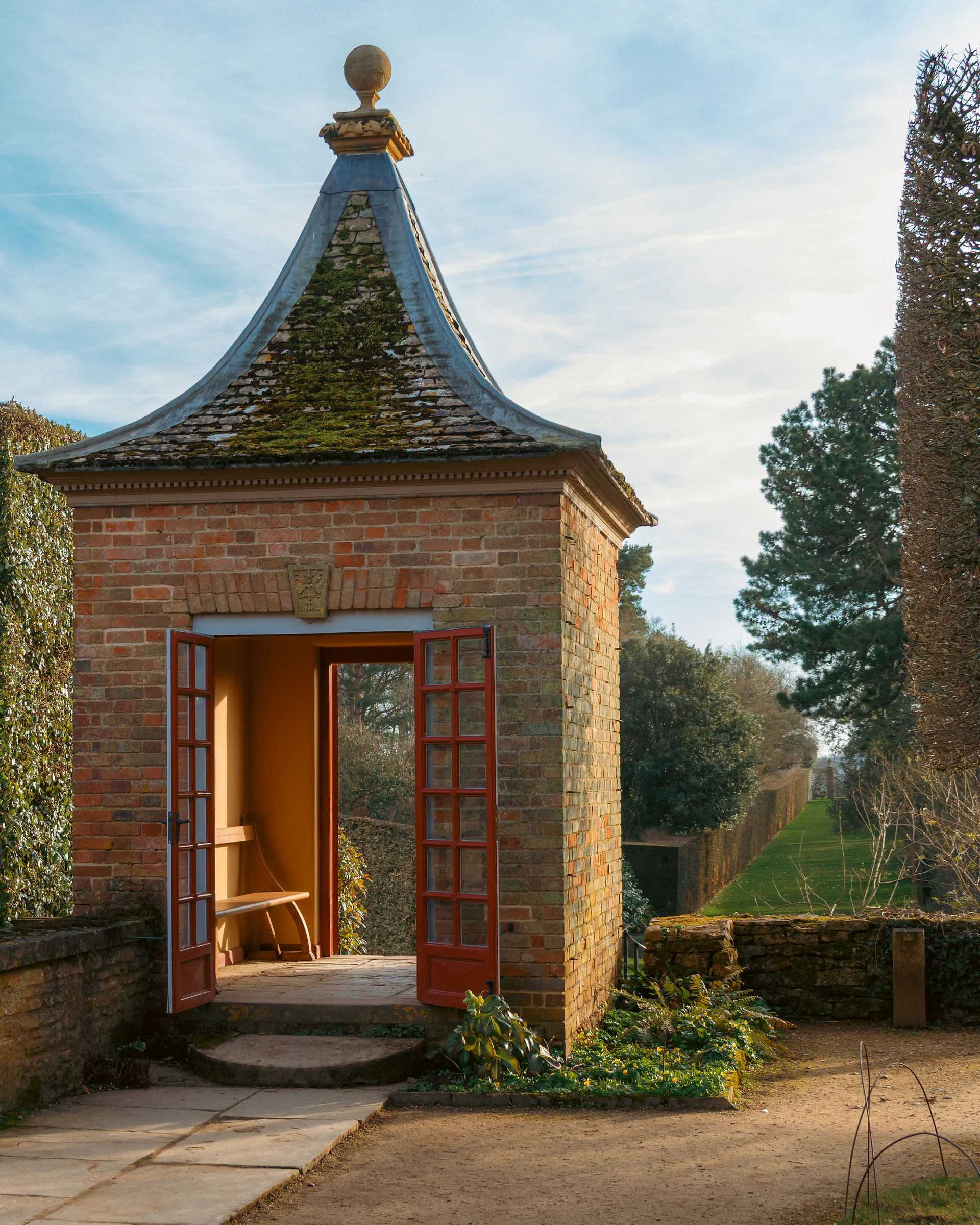 A red brick Gazebo building with  a turquoise roof against a blue sky 