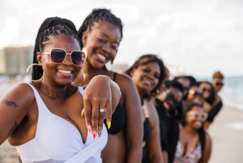 Engagement ring detail with a group of friends celebrating together in the background.