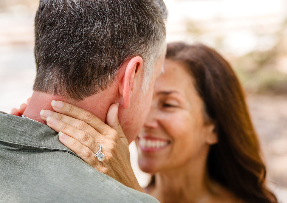 Close-up of a newly engaged woman embracing her partner with her engagement ring visible over his shoulder.