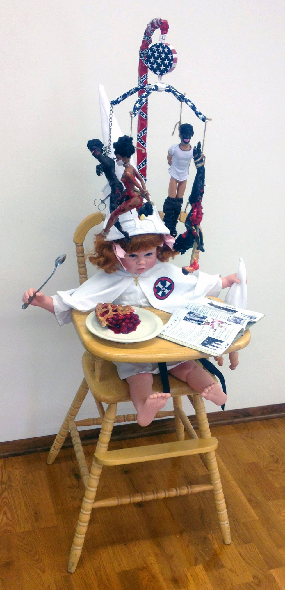Lili Bernard. As American as Cherry Pie, 2014. Baby doll parts, Barbies, highchair, baby mobile, nails, cotton fabric, rope, chain, scissors, digital photos, children’s book, acrylic paint, 60 x 40 x 30 inches