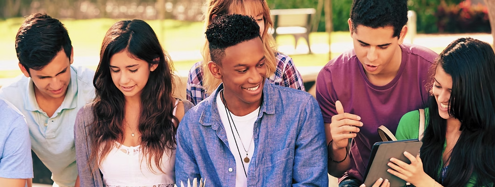 A group of teenagers sitting outdoors, smiling and looking at a tablet together while talking and enjoying each other’s company.