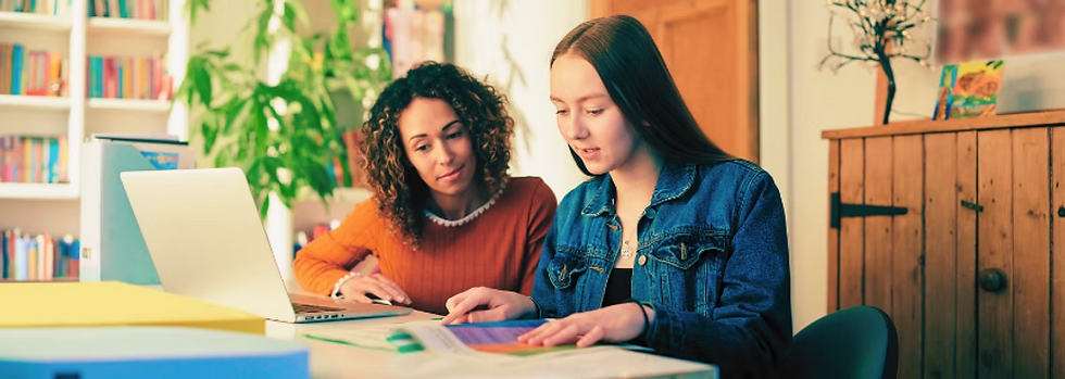 Tutor working with a teenage student at a table, reviewing schoolwork together with a laptop and books, representing personalized learning support for students with ADHD.