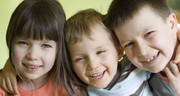 Three cheerful children are posing for the camera, all smiling brightly.