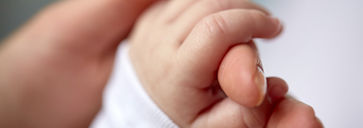 An adult's hand envelops a baby's hand, illustrating a bond of safety and love between them.