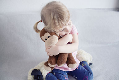 A small girl cuddles a stuffed monkey, highlighting a tender moment of companionship and joy.