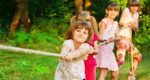 Children joyfully playing with a rope on green grass, engaging in a fun outdoor activity together.