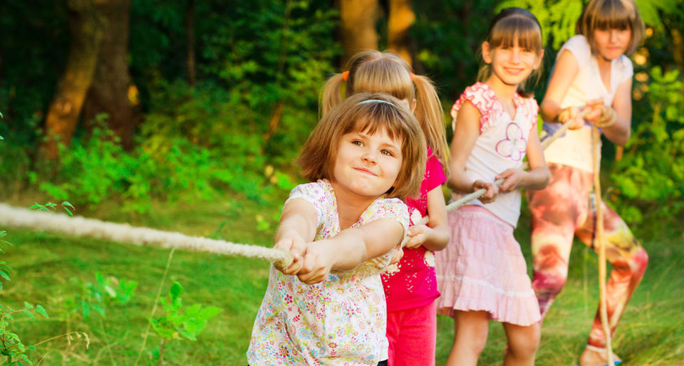 Children joyfully playing with a rope on green grass, engaging in a fun outdoor activity together.
