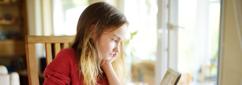 A girl comfortably seated at home, using a tablet for learning or entertainment.