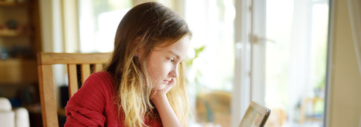 A girl comfortably seated at home, using a tablet for learning or entertainment.