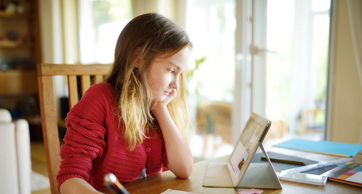 A girl comfortably seated at home, using a tablet for learning or entertainment.