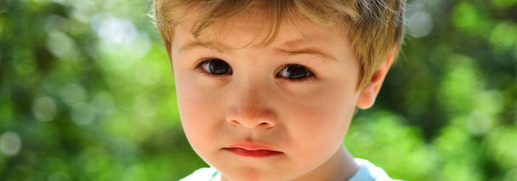 A young boy looks at the camera with a sorrowful face, reflecting his feelings of sadness.