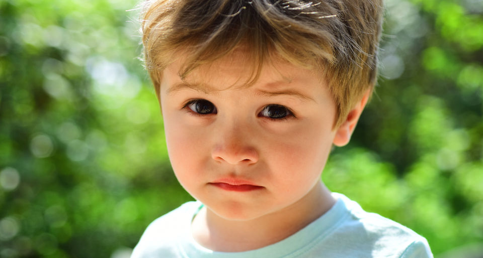 A young boy looks at the camera with a sorrowful face, reflecting his feelings of sadness.