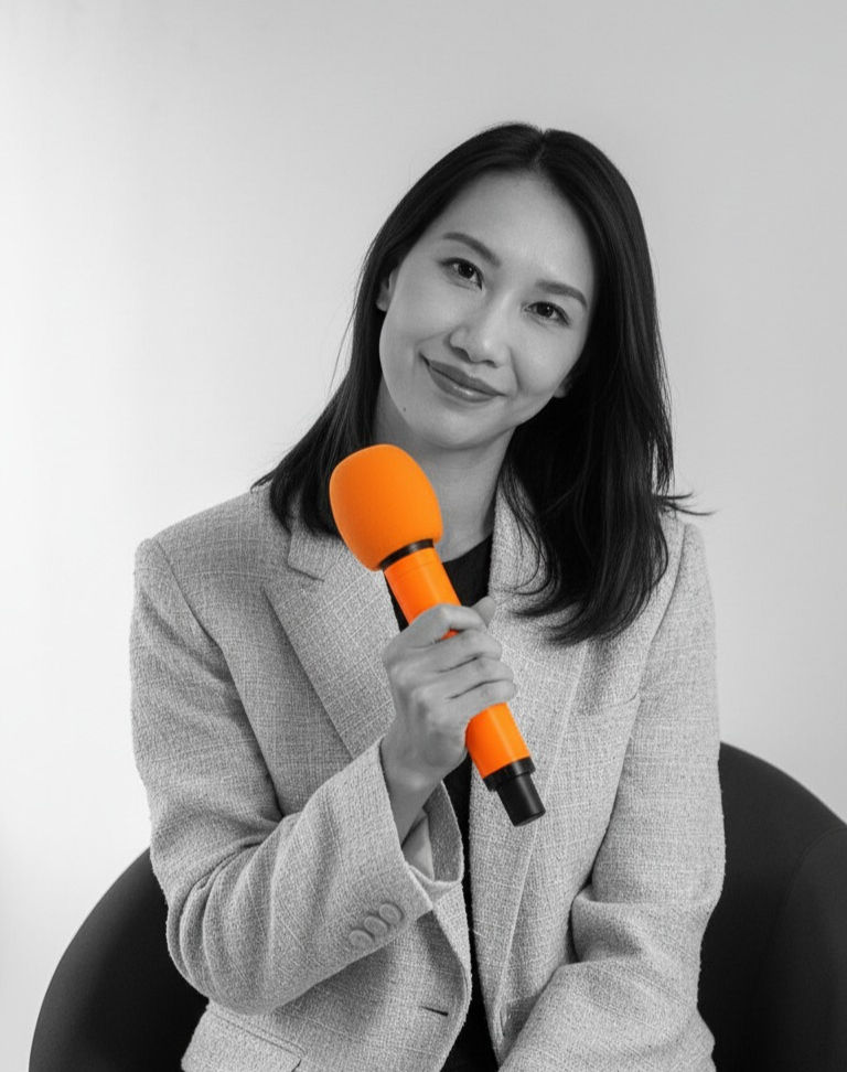 譚巧燕 Catherine Tam Thillanathan,Prosci 的高階講師、ChangeAccomplishment 的首席顧問、睿變圈的共同創辦人,坐在椅子上,手持橙色麥克風,展現出自信和親和力。