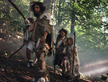 Prehistoric group in fur clothing walks through a sunlit forest, holding wooden spears, evoking a sense of adventure and survival.