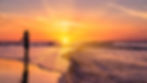 Sunset over a beach with a woman walking on the shore