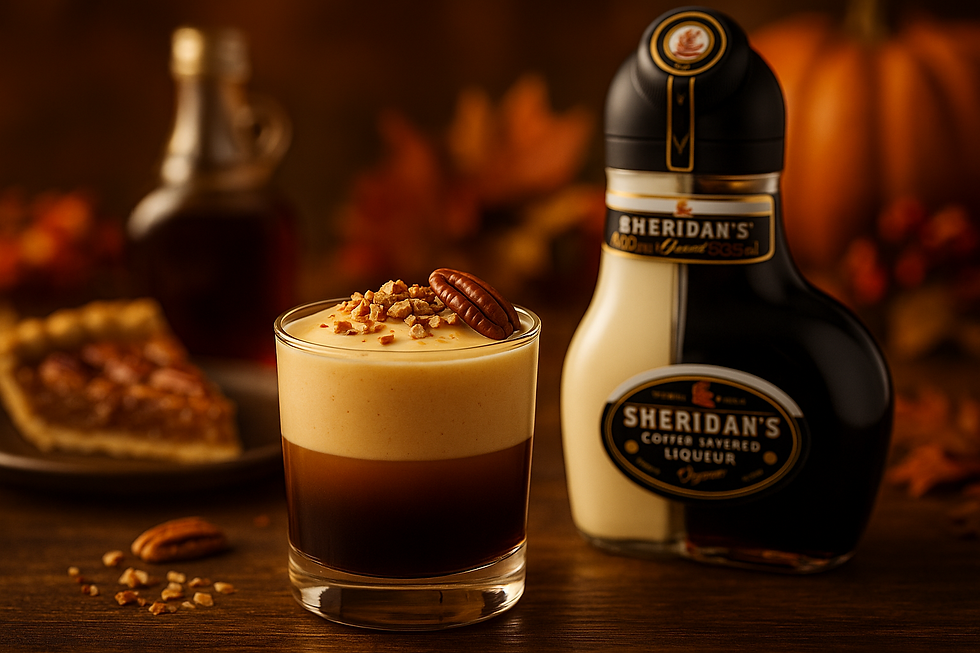 Glass of layered coffee with cream and nuts, next to a Sheridan's bottle. Background includes syrup and pecan pie on a warm, autumnal table.