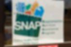Sign for SNAP, Supplemental Nutrition Assistance Program, featuring grocery items in a bag. Text: Putting Healthy Food Within Reach.