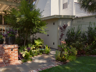 Garden with brick and bluestone path and lush green beds with texture and color. 