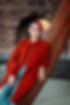 An image of Lindsay wearing a long rust colored sweater and scarf, leaning against a tall metal sculpture in the Richardson Complex.