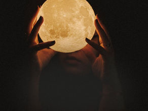 A small glowing moon ball being held by a woman in front of her face.