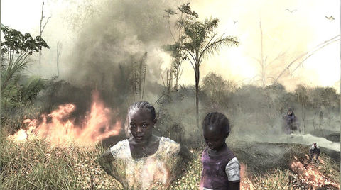 Two African girls standing in front of a burning forest with smoke that they have started.