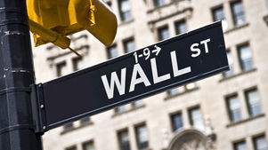 Wall St street sign beside a yellow traffic light, with a blurred city building in the background.