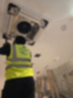 Technician in a safety vest repairing a ceiling AC unit.