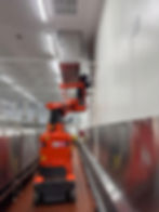 Worker on an orange lift in a facility gallery.