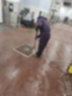 Worker pressure washing a floor drain in a gallery.