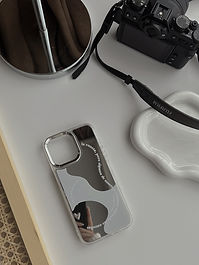 Elegant Mirror phone case adorned with white accents and an inspiring quote by Oscar Wilde: 'We are all in the gutter, but some of us are looking at the stars.' A minimalist design that encourages us to dream big and find beauty in the unexpected. Elegant Phone case next to camera and jewelry tray
