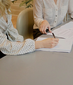 woman signing on white printer paper beside woman about to touch the documents_edited.jpg
