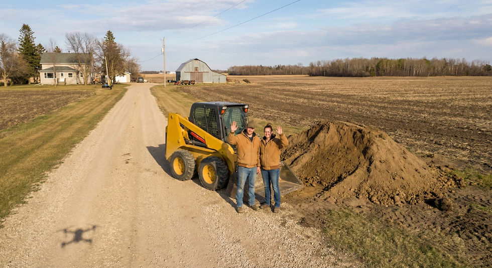 home owners waving at a camera on a rural property in front of a skidsteer