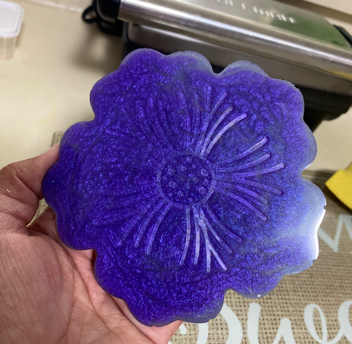 Hand holding a purple flower shaped coaster,