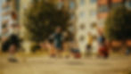Kids playing street soccer on a sunny day in an urban playground with apartment buildings and trees. The mood is lively and joyful.