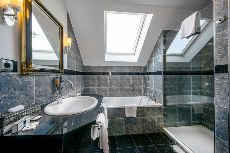 Geräumiges Badezimmer mit Dusche und separater Badewanne. Dunkelgraue Fließen verleihen dem Badezimmer eine elegante Note. Hygieneartikel wie Seife und Duschgels sind vorhanden.