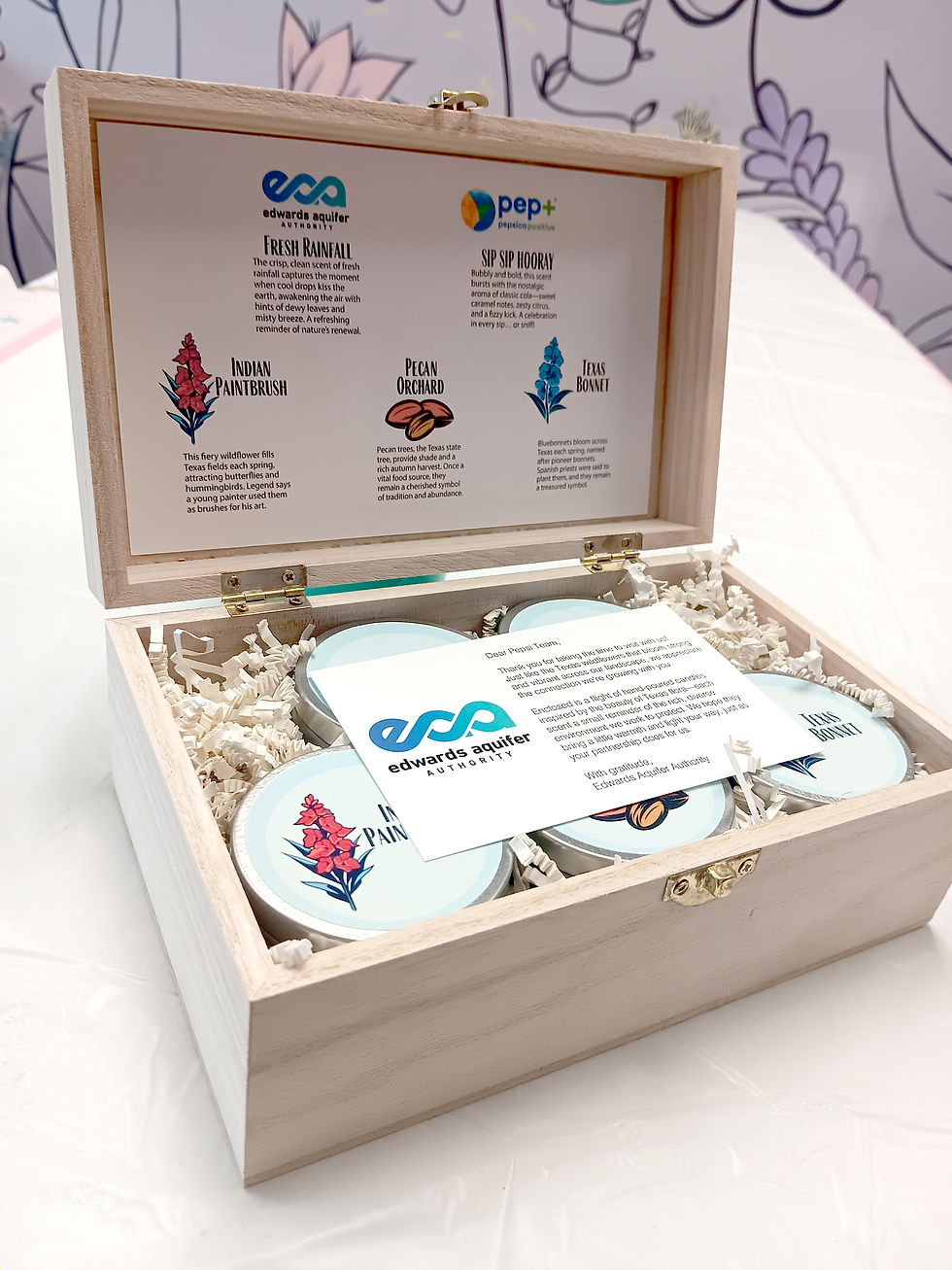 Wooden box with jars labeled "Indian Paintbrush," "Pecan Orchard," "Texas Bonnet" on shredded paper. Card with Edwards Aquifer logo inside.