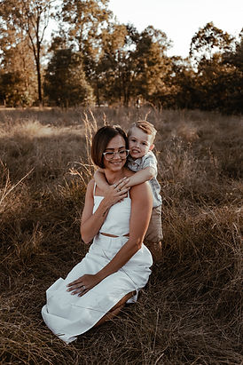 Motherhood mother and son cuddling in a long grass field in Greenbank for a sunset family motherhood session neutral toned natural candid photography outdoor on location
