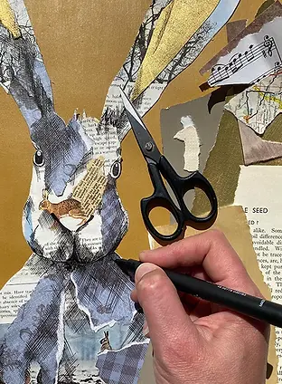 Original handcrafted hare collage in progress on the studio desk, with a hand placing final detail amongst scissors, tools and layered materials.