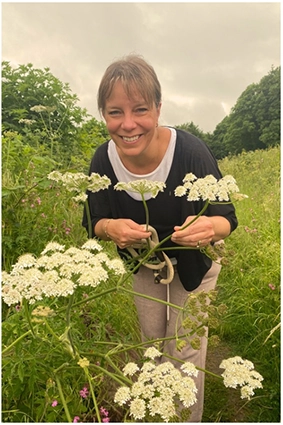 Louise standing outdoors on a walk, holding a stem of cow parsley in her hands.