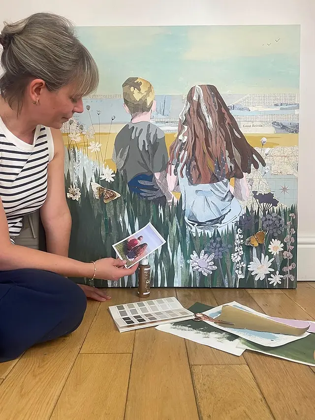 Louise looking at a photograph beside a large collaged artwork in the studio..