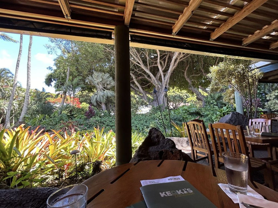 An interior dining view of Keoki's Paradise with wood beam ceiling, tropical garden views, set tables, and ambient natural light.