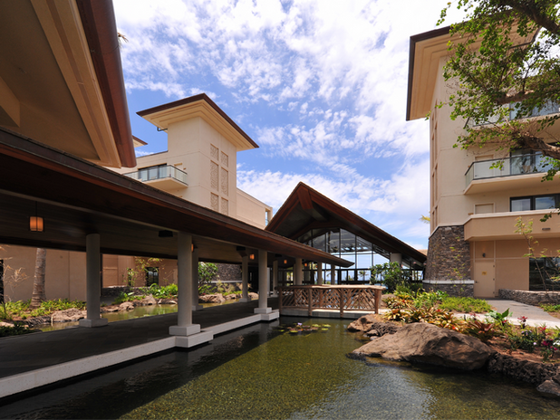 Covered Walkway Over Water Feature – A serene covered bridge extending over a koi pond, surrounded by tropical plants and elegant resort architecture.
