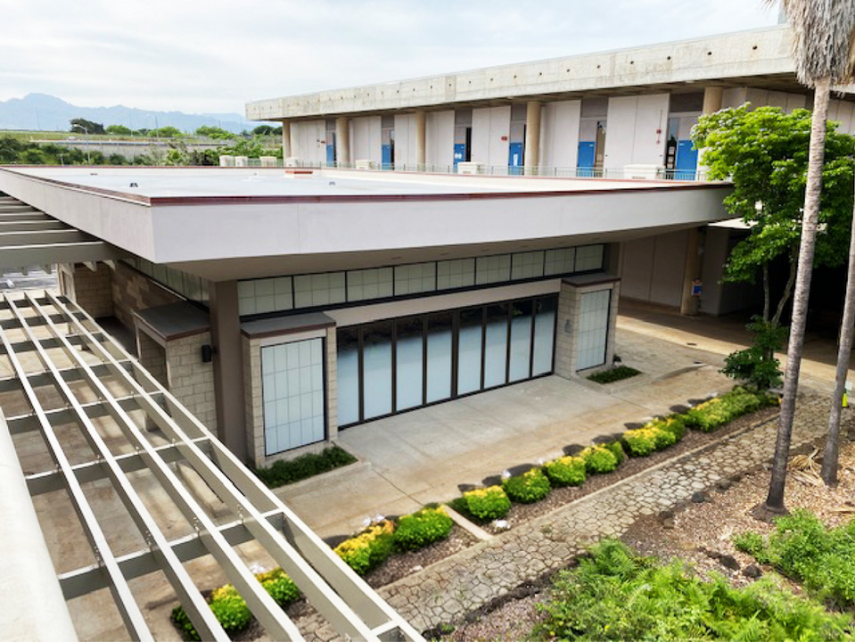 Exterior of a low-rise educational building with a flat roof, large windows with blue accents, an overhead trellis, and drought-tolerant landscaping.