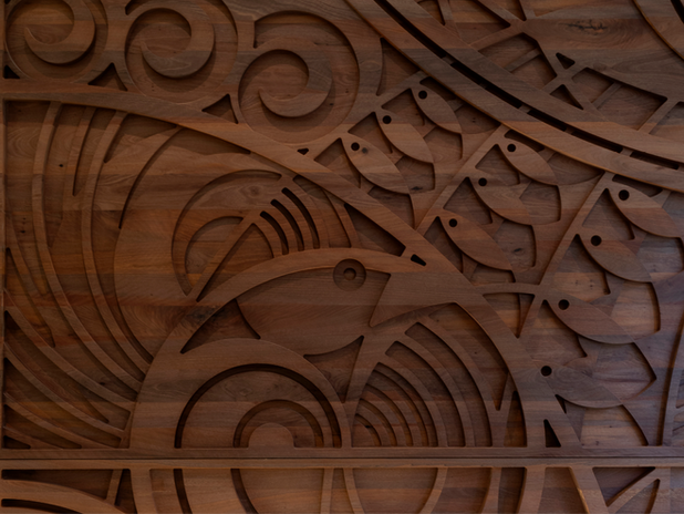  (Wood Carving) – A detailed wooden panel with intricate Polynesian-inspired carvings. The design includes a stylized bird, swirling patterns, and leaf-like shapes, creating a rich cultural motif.