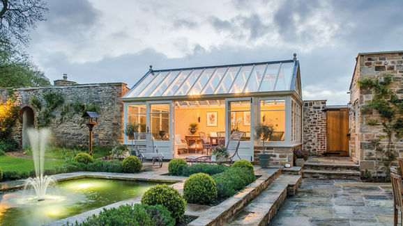 Large orangery with full-height glass, internal lights glowing, and garden fountain in foreground