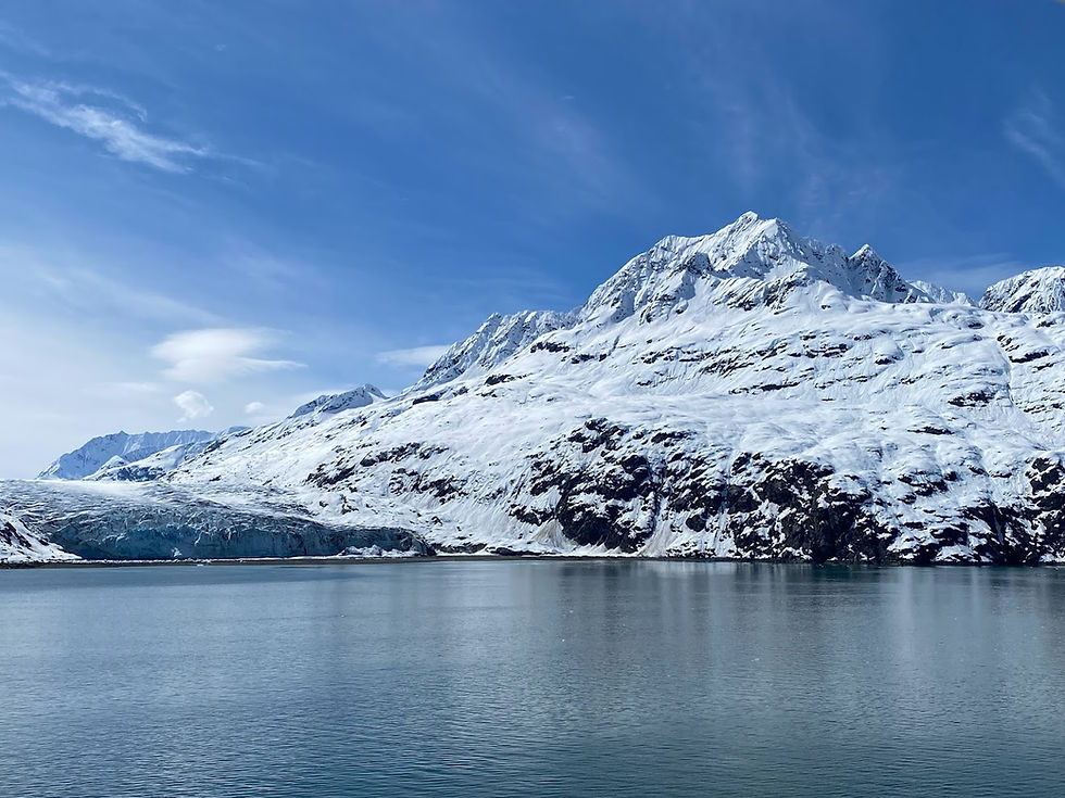 Glacier Bay National Park under a bright blue sky, reflected in a calm body of water. The scene is serene and majestic.