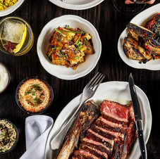 Image of several dishes on a table. The main dish appears to be medium rare steak