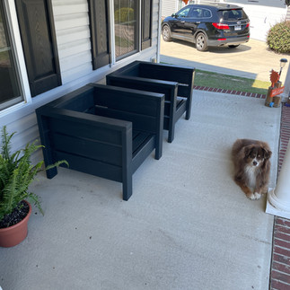 A set of two black outdoor chairs, set on the front porch.